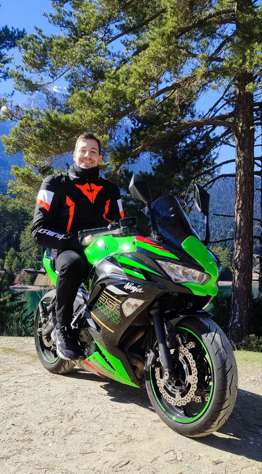 Konstantinos Tsounidis smiling on his green Kawasaki Ninja by a mountain lake